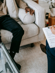 man sitting on couch with therapist across from him with check list and pen